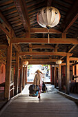 A woman carrying bags on a hod through the covered Japanese bridge in Hoi An, Quang Nam, Vietnam, Indochina, Southeast Asia, Asia