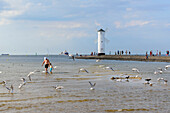 Father with child in shallow water. The mill beacon stands on the west pier and shows the ships the entrance to the Swine, Swinoujscie, Ostseeküste, Poland