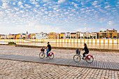 People cycling by the river Rio Guadalquivir, with Triana district in the background, Seville, Andalusia, Spain, Europe