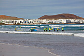 Surfer am Playa de Famara und die Ortschaft La Caleta de Famara, Atlantik, Lanzarote, Kanaren, Kanarische Inseln, Islas Canarias, Spanien, Europa