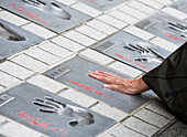A womans hand touching a memorial plaque along the sidewalk near the Asakusa Kannon Temple.