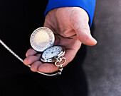 A close up of a man's hand holding a open pocket watch.