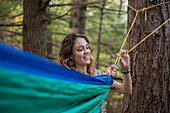 Smiling woman setting up hammock in forest