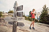 A woman consults her trail map next to a trail sign while hiking in Acadia National Park, Maine.