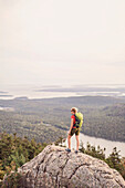 An active woman takes in in the view of the Atlantic Ocean from the summit of Pemetic Mountain in Maine's Acadia National Park.