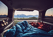 Bedrolls inside car with mountain range visible in background, Wyoming, USA