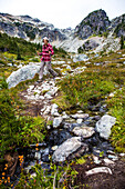 A woman hikes through Brandywine Meadows, an alpine meadow very popular in the winter for backcountry snowmobiling, an a fall day and takes in the picturesque view of the surrounding mountains. Whistler, British Columbia, Canada