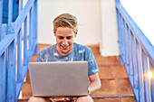 Happy handsome man in leisure clothes using mobile computer laptop