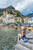 Amalfi, Amalfi coast, Salerno, Campania, Italy. Young woman sitting on the pier of Amalfi village