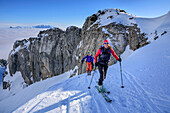 Three persons backcountry skiing ascending beneath rockface towards Hinteres Sonnwendjoch, Hinteres Sonnwendjoch, Bavarian Alps, Tirol, Austria