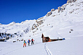 Drei Personen auf Skitour gehen auf Almhütte zu, Peitlerkofel, Naturpark Puez-Geisler, UNESCO Weltnaturerbe Dolomiten, Dolomiten, Südtirol, Italien