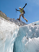 A mountain climber is jumping over a crevasse on Mer de Glace, a famous glacier in the Mont Blanc range.