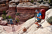 Three female backpackers follow cairns down into Maze part of Canyonlands National Park, Moab, Utah, USA
