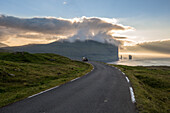 car following a winding road at sunset, cliffs and ocean in the background, eidi, eysturoy, faroe islands, denmark