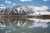 hiker near a lake at the foot of the snow-covered peaks, tavan bogd massif, altai, bayan-olgii province, mongolia