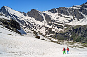 Mann und Frau beim Wandern steigen durch Schnee zum Refuge Viso ab, Giro di Monviso, Monte Viso, Monviso, Cottische Alpen, Frankreich