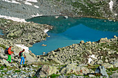 Mann und Frau beim Bergsteigen gehen auf herzförmigen See Lago Chiaretto zu, Giro di Monviso, Monte Viso, Monviso, Cottische Alpen, Piemont, Italien