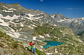Man and woman hiking ascending from heart-shaped lake lago Chiaretto, Giro di Monviso, Monte Viso, Monviso, Cottian Alps, Piedmont, Italy