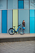 junge Frau auf eBike vor moderner Glasfassade, München, Bayern, Deutschland