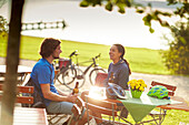 Young  woman and young man on bicycletour sitting in beergarden, Muensing, Lake Starnberg;  bavaria, germany