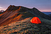 Orangenes Zelt auf  auf einem Bergrücken im warmen Morgenlicht der aufgehenden Sonne, Hofn, Vesturland, Island