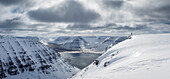 Ski alpinist standing on top of a table mountain and enjoys the view over the fjord landscape, West fjords, Iceland