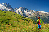 Woman hiking on path through meadow with view towards Meije in Ecrins region, National Park Ecrins, Dauphine, Dauphiné, Hautes Alpes, France