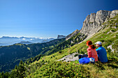 Frau und Mann beim Wandern sitzen auf Wiesenabsatz und blicken auf die Bergkulisse, am Grand Veymont, Vercors, Dauphine, Dauphiné, Isère, Frankreich