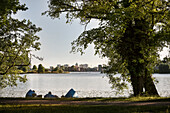 people relaxing and enjoying the view from waterside of royal garden Glienicke at city with chapel of St Nikolai church, Potsdam, Brandenburg, Germany
