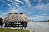 Ein Holzhaus auf Stelzen mit Palmblattdach steht in einer Lagune unter leicht bewölktem blauem Himmel, Butaritari Atoll, Gilbert-Inseln, Kiribati, Südpazifik