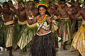 Eine breit lächelnde Frau in traditioneller Kleidung tanzt vor einer großen Gruppe von Männern in traditioneller Kleidung, Butaritari Atoll, Gilbert-Inseln, Kiribati, Südpazifik