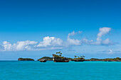 Tiny craggy islands, some crowned with palm trees, stand in front of larger islands in the background, all surrounded by turquoise water, Fulaga Island, Lau Group, Fiji, South Pacific