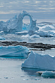 Einer der zahlreichen Eisberge weist einen unwahrscheinlich aufragenden, mindestens 20 Meter hohen Torbogen auf, Pleneau Island, Wilhelm Archipelago, Antarktis