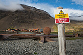 A prominent sign warns of the asbestos hazard in a no-go area strewn with huge, rusty propellers, scrap metal, tanks and distant dilapidated buildings, all that remains after decades of whaling, Stromness, South Georgia Island, Antarctica