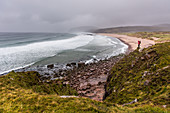 Eine Wanderin steht auf einem Hügel am Strand der Sandwood Bay, Highlands, Schottland, Großbritannien