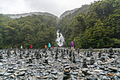Tourists walking through rock cairns at Fantail Falls on a rainy day. Mount Aspiring National Park, West Coast region, South Island, New Zealand.