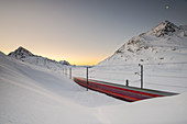 The Bernina Express train runs along the Lake Bianco complete cover of snow before the sunrise, Bernina Pass with some bubbles, Canton of Graubuden, Engadine, Switzerland, Europe