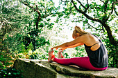 Woman stretching on rock in forest