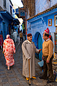 Street scene, old man with stick and red fez (hat) stops to talk with a the owner of a bookshop, Chefchaouen, Morocco, North Africa, Africa