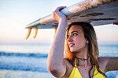 Frau in gelbem Bikini mit Surfbrett am Strand