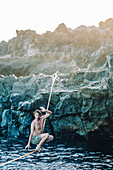 Young shirtless man balancing across tightrope over coastal water,†Tenerife, Canary Islands, Spain