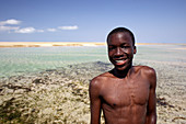 Portrait of shirtless boy standing on coastal beach and smiling, Mozambique