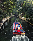 A man drives a water taxi along the San Antonio river walk on a sunny late summer day. The riverwalk is covered with a canopy of trees and makes for a nice peaceful place to walk.