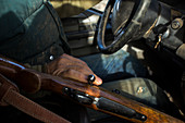 Mid section of person sitting behind wheel and touching rifle lying on passenger seat, Grass Valley, Oregon, USA