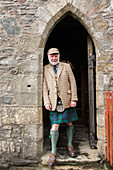 Mann in traditionellem Kilt steht im Torbogen von Eilean Donan Castle, Schottland, Großbritannien