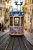 Painted tram waiting on rails across steep city street, Lisbon, Portugal