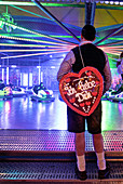 Man with big gingerbread heart in front of bumper cars on the Oktoberfest, Munich, Bavaria, Germany