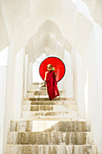 Asian Buddhist monk carrying umbrella on staircase at Hsinbyume Pagoda, Mandalay, Sagaing, Myanmar