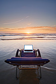 Laptop auf Liegestuhl mit Blick auf den Sonnenuntergang am Strand