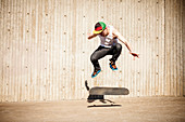 Caucasian man doing skate trick near wooden wall